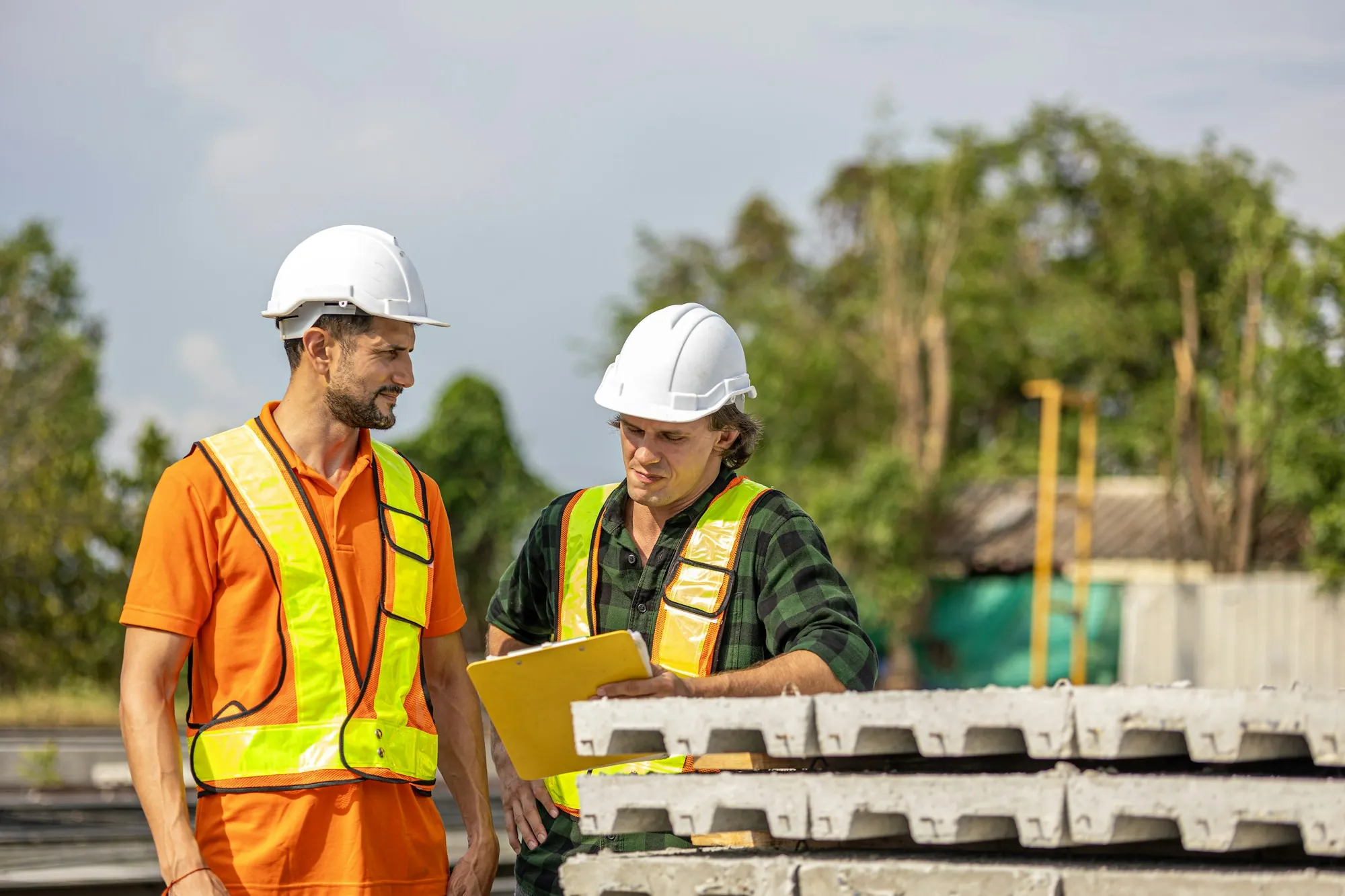 Two electricians in hard hats reviewing a plan on a clipboard