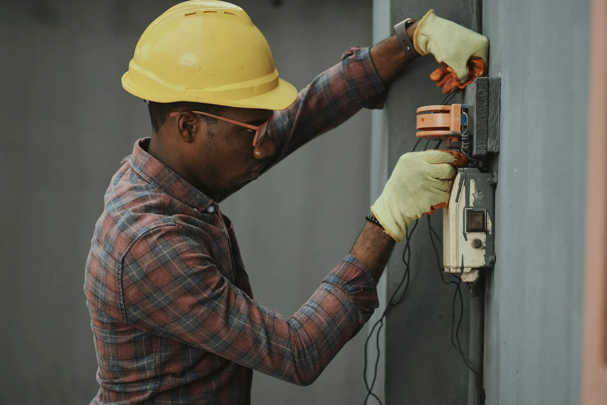 Electrician in a hard hat working at a wall-mounted electrical box
