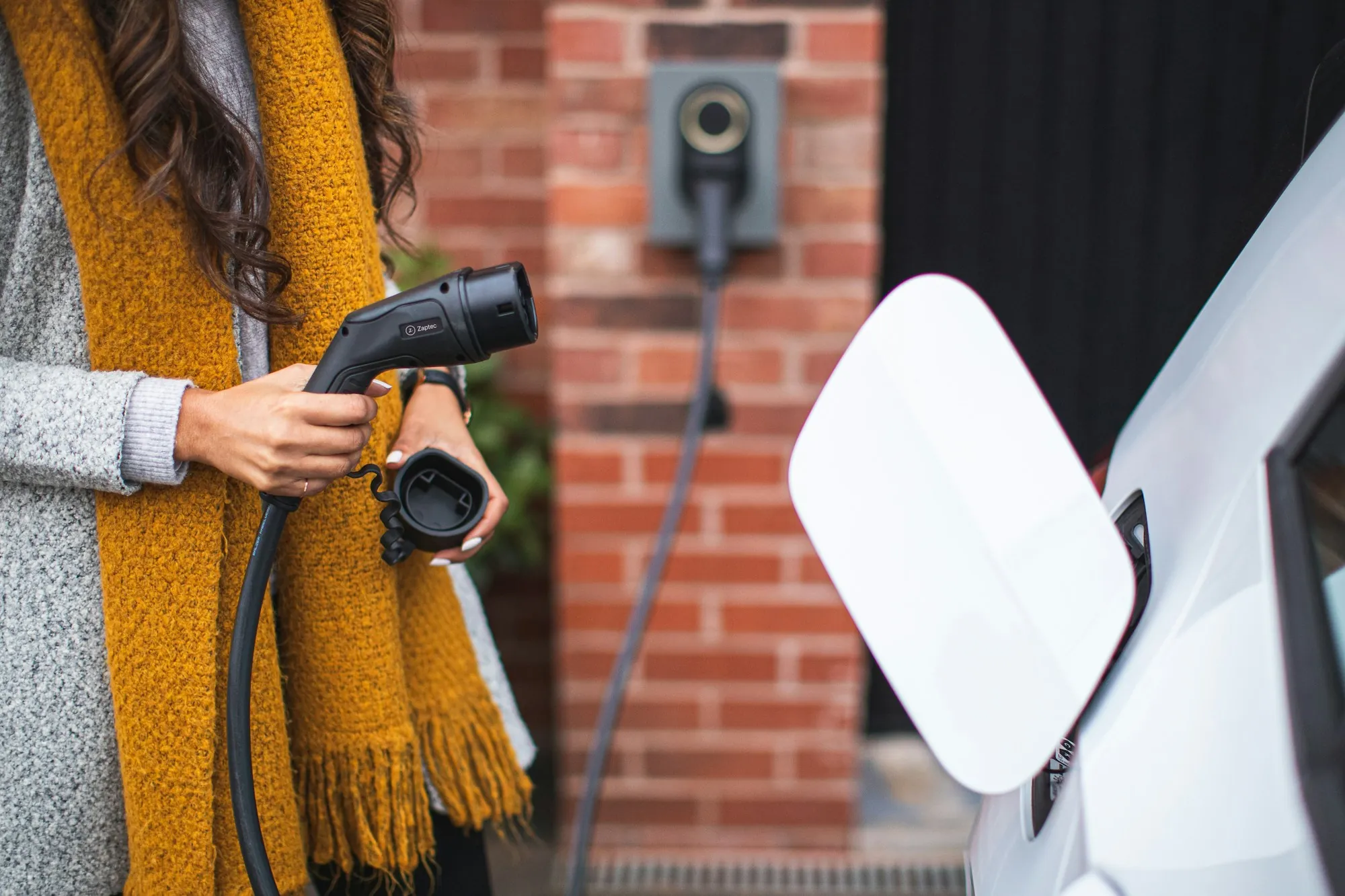 Woman holding an EV charging connector beside a wall charger